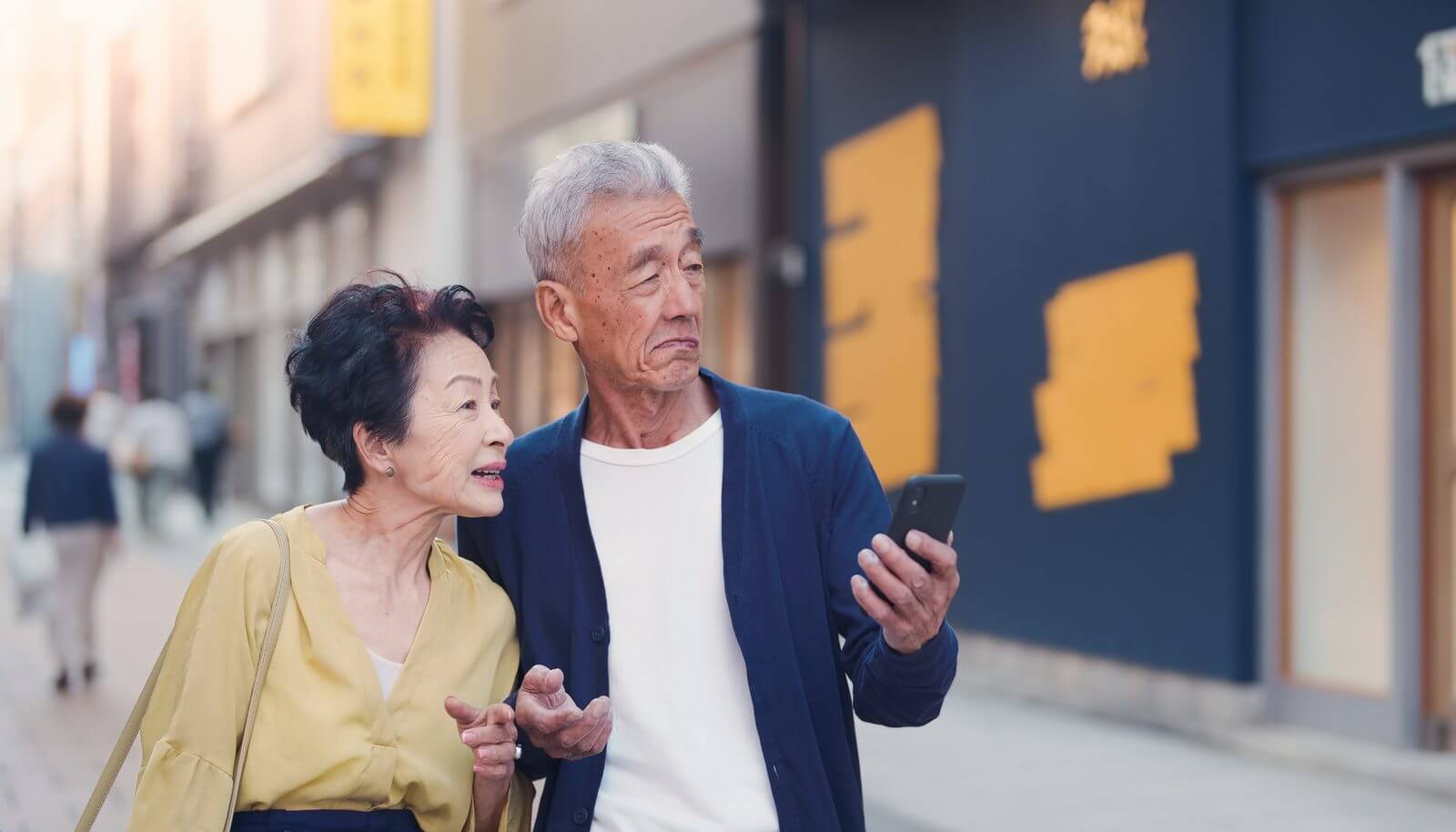 補聴器をどこで買えばいいか、商店街でスマートフォンを見ながら迷う高齢の夫婦
